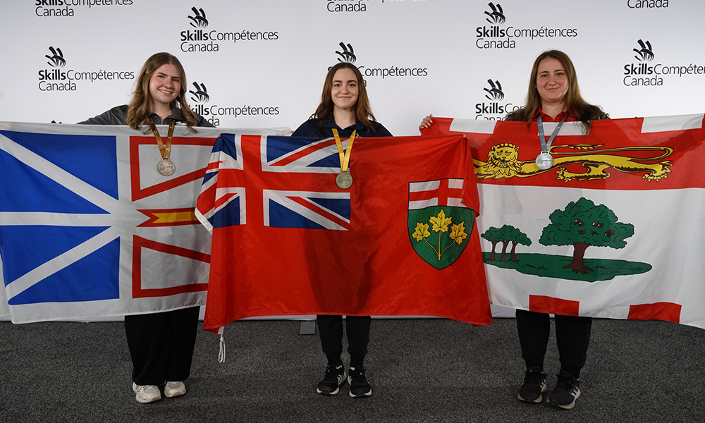 Emili Bykovsksi stands alongside recipients of gold and bronze awards. Each holds their provincial flag outstretched.