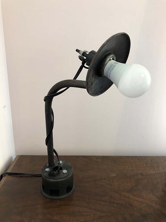 A black rustic lamp welded from pipes and other scrap materials sits on a wooden desk